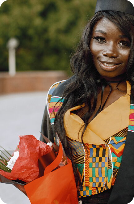 An FGC Kano graduate in cap, gown and kente stole holding a bouquet