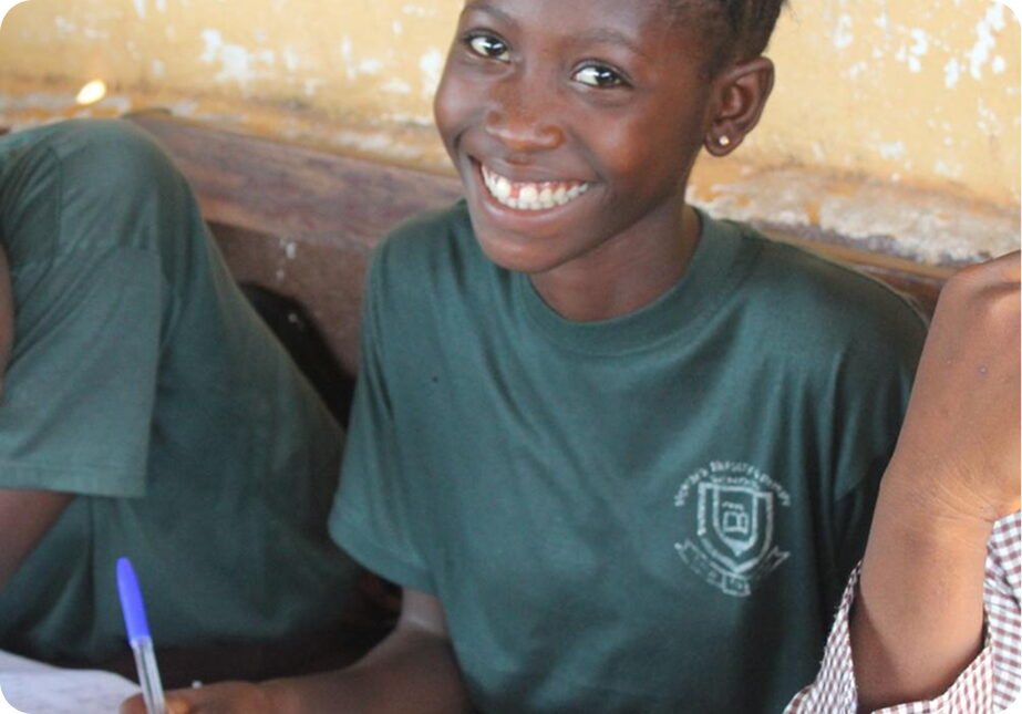 A smiling student in a green FGC Kano uniform holding a pen over her notebook